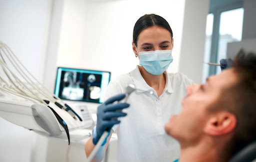 Female dentist wearing a mask prepares to clean a male patient�s teeth with a dental X-ray visible behind them